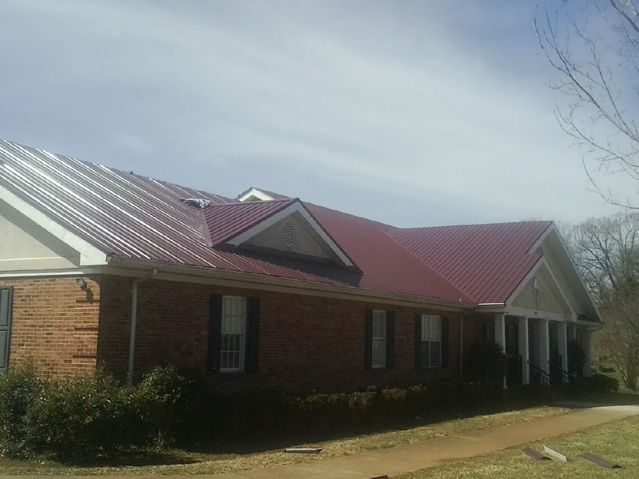Red metal roof with gabled entries on a long brick building, from a Hail Damage Roof Repair job in Monroe Township