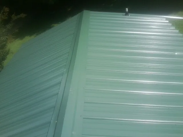 New green metal panels meeting at the ridge of a roof — Flat Roof Repair work by our crew in Monroe Township