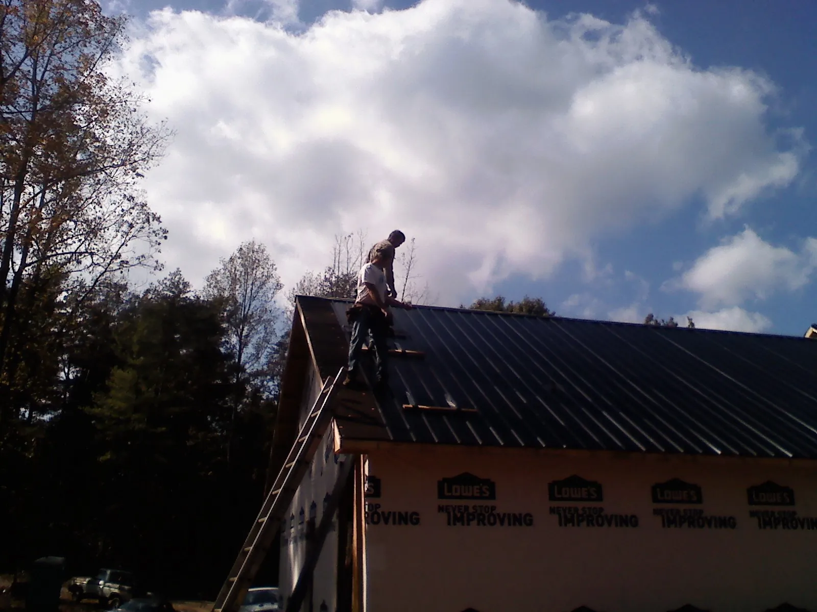 Roofer fastening dark metal panels high against a cloudy sky, from a Roof Inspection job in Monroe Township