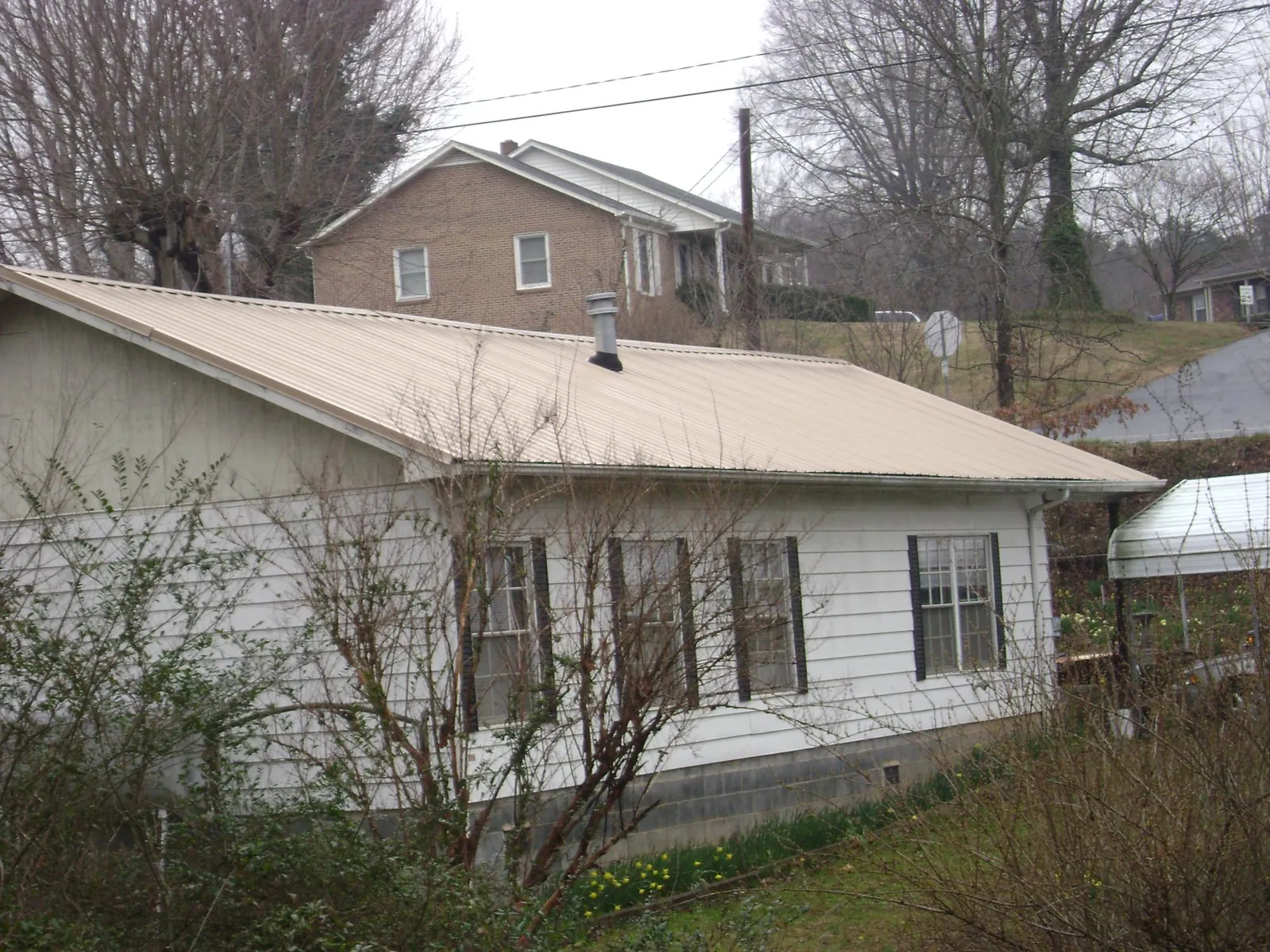 Tan metal roof on a white sided house set into a hillside — Commercial Roofing by Roofing Brothers in Monroe Township